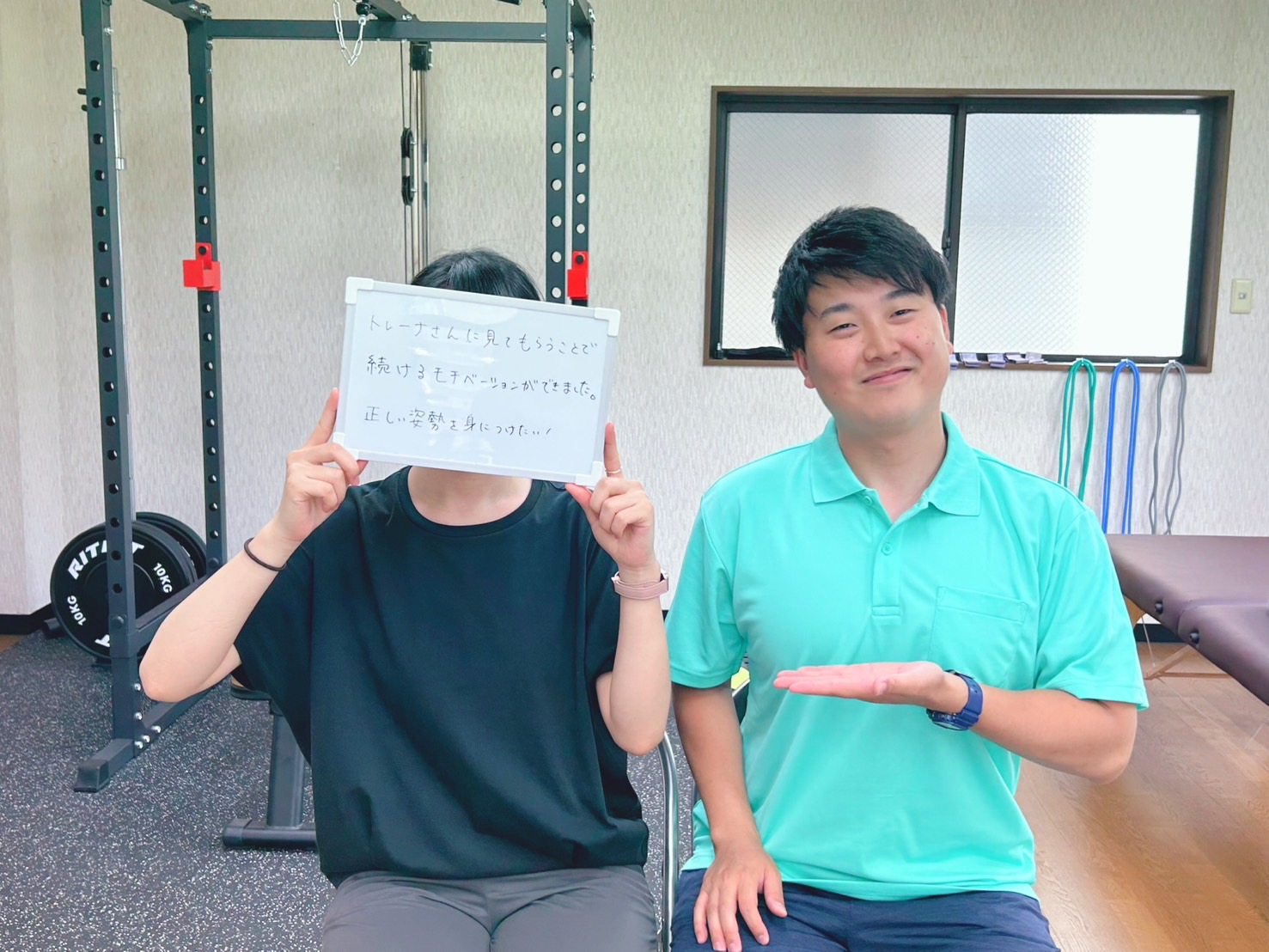 トレーナーとクライアントが写っているジムの内部。クライアントはボードを持っていて、トレーナーは笑顔で手を差し出している。